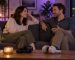 Two adults talking together on a sofa with headphones nearby.
