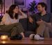 Two adults talking together on a sofa with headphones nearby.